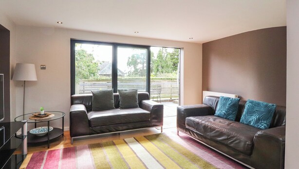 A modern living room with two leather sofas, a glass coffee table, and a colorful striped rug. - Underfell (Carnforth)