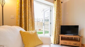 Una sala de estar con un sofá blanco, una almohada amarilla, un televisor sobre un soporte de madera y cortinas amarillas con estampado.