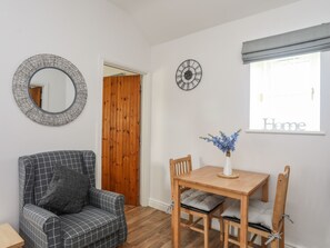 Ein Zimmer mit einer karierten Couch, einem Holzespeisetisch mit Stühlen, einem Spiegel, einer Uhr und einem Fenster mit einem Schild mit der Aufschrift 'Home'.