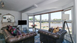 A living room with two leather sofas, a flat-screen TV, a table with a vase, and large windows overlooking a body of water. - Sea View Apartment (Porthmadog)