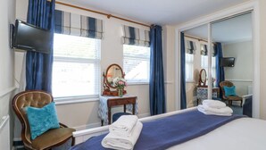 A hotel room with a bed, a chair, a vanity with a mirror, a TV, and a window with curtains. - Sea View Apartment (Porthmadog)