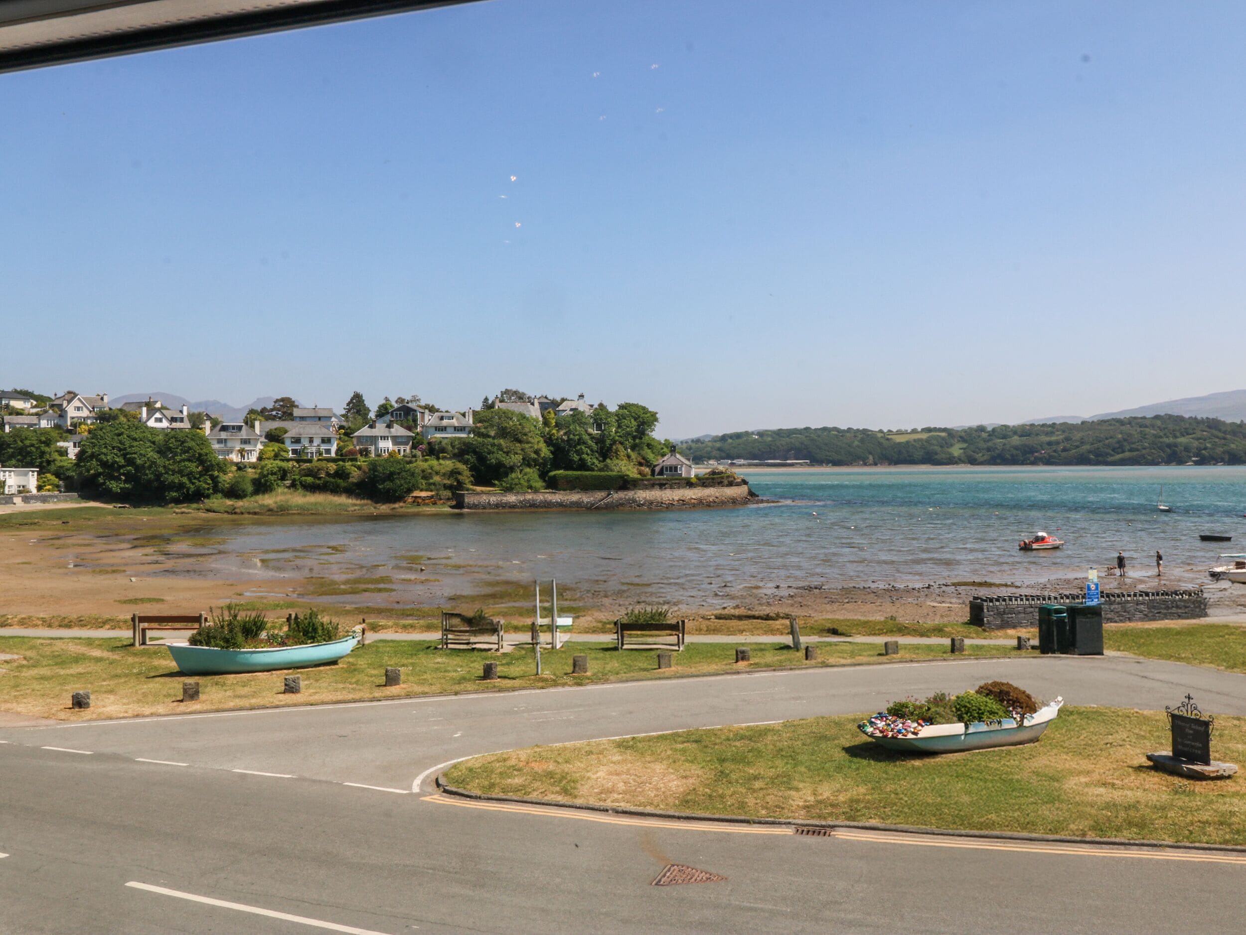 A coastal road with a view of a lake, houses, and a boat-shaped planter.