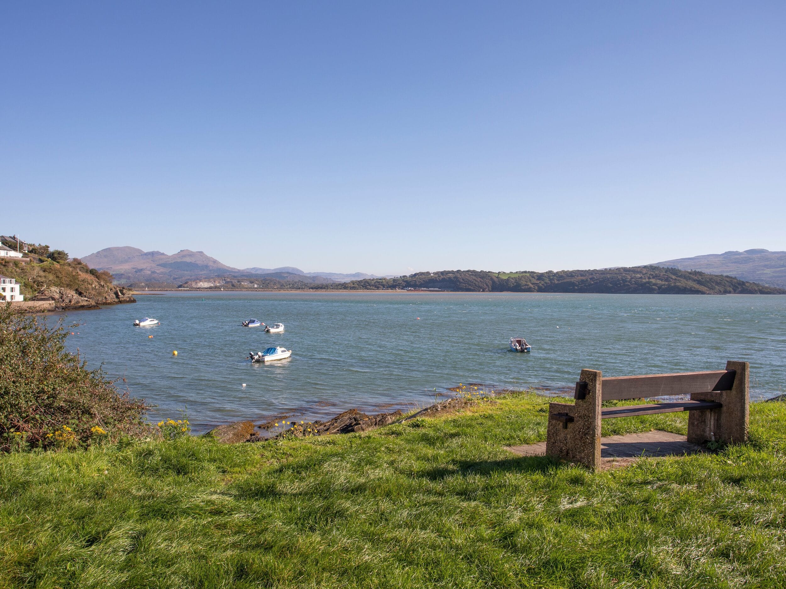 A lakeside view with boats, a grassy area, and a wooden bench.