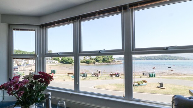 A room with a large bay window overlooking a beach and water. - Sea View Apartment (Porthmadog)