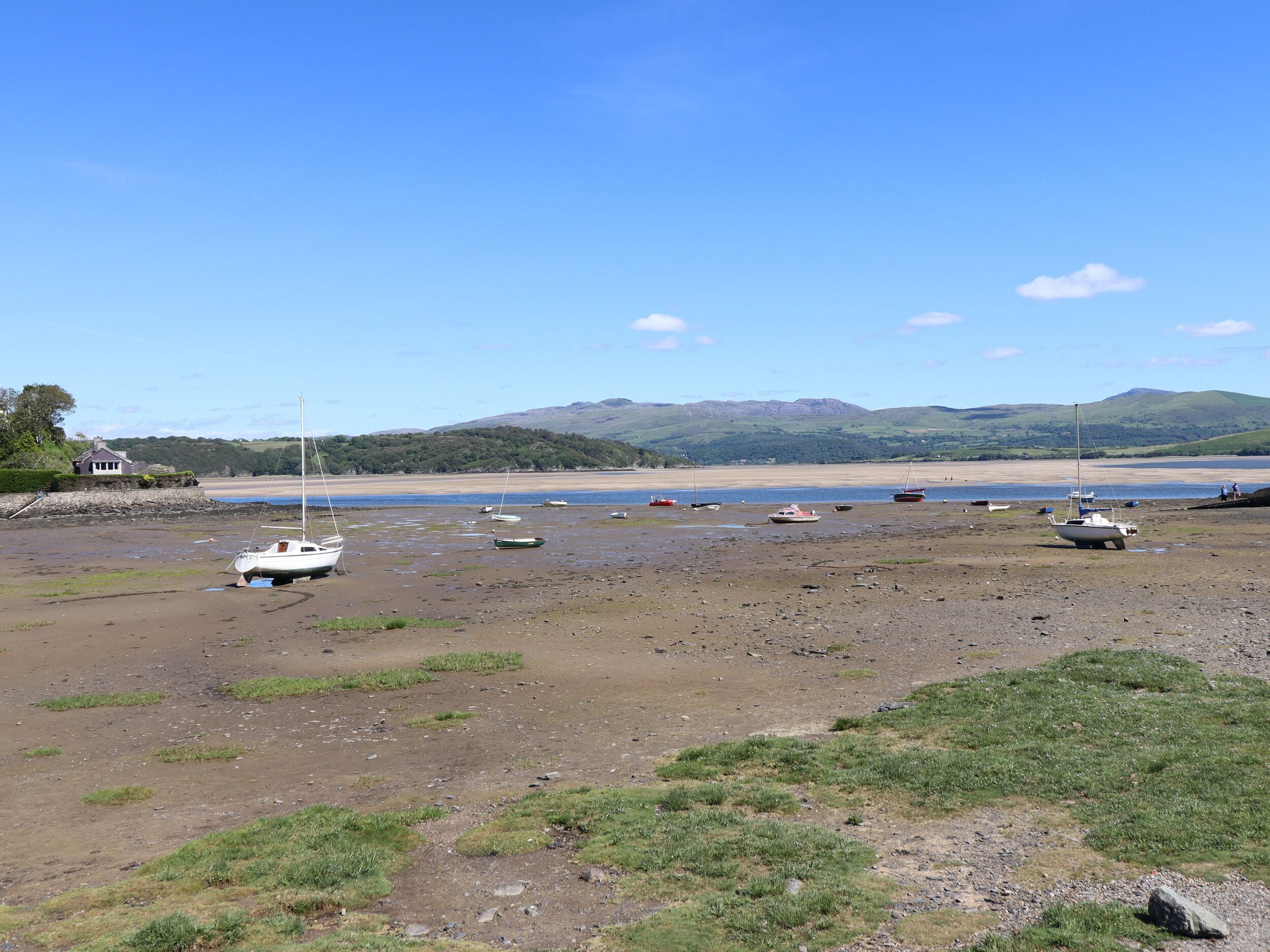 A coastal landscape with boats on a sandy beach, a house, and hills in the background.
