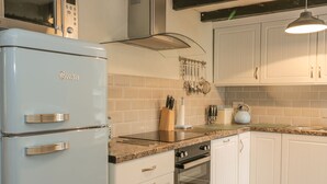 Une cuisine avec des meubles blancs, un réfrigérateur bleu, un four à micro-ondes et une cuisinière.