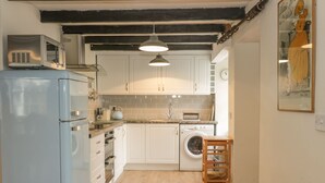 Une cuisine de taille réduite avec des meubles blancs, un réfrigérateur bleu, un lave-linge et un tabouret en bois.