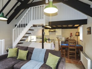 A cozy living room with a brown sofa, green cushions, a staircase, and a kitchen area.