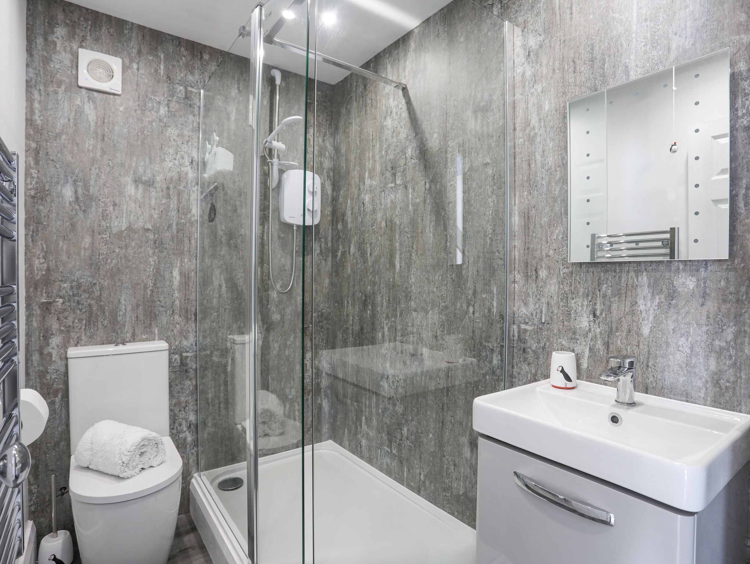 Une salle de bain moderne avec une douche à parois de verre, des toilettes blanches et un lavabo surmonté d’un miroir.