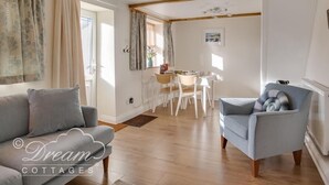 A cozy living room with a grey sofa, a blue armchair, and a dining area with a white table and chairs. - Ammonite Cottage (Portland)