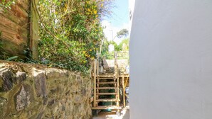 Ein schmaler Gang mit einer Steinmauer an einer Seite und einer Holztreppe, die zu einer höheren Ebene führt.