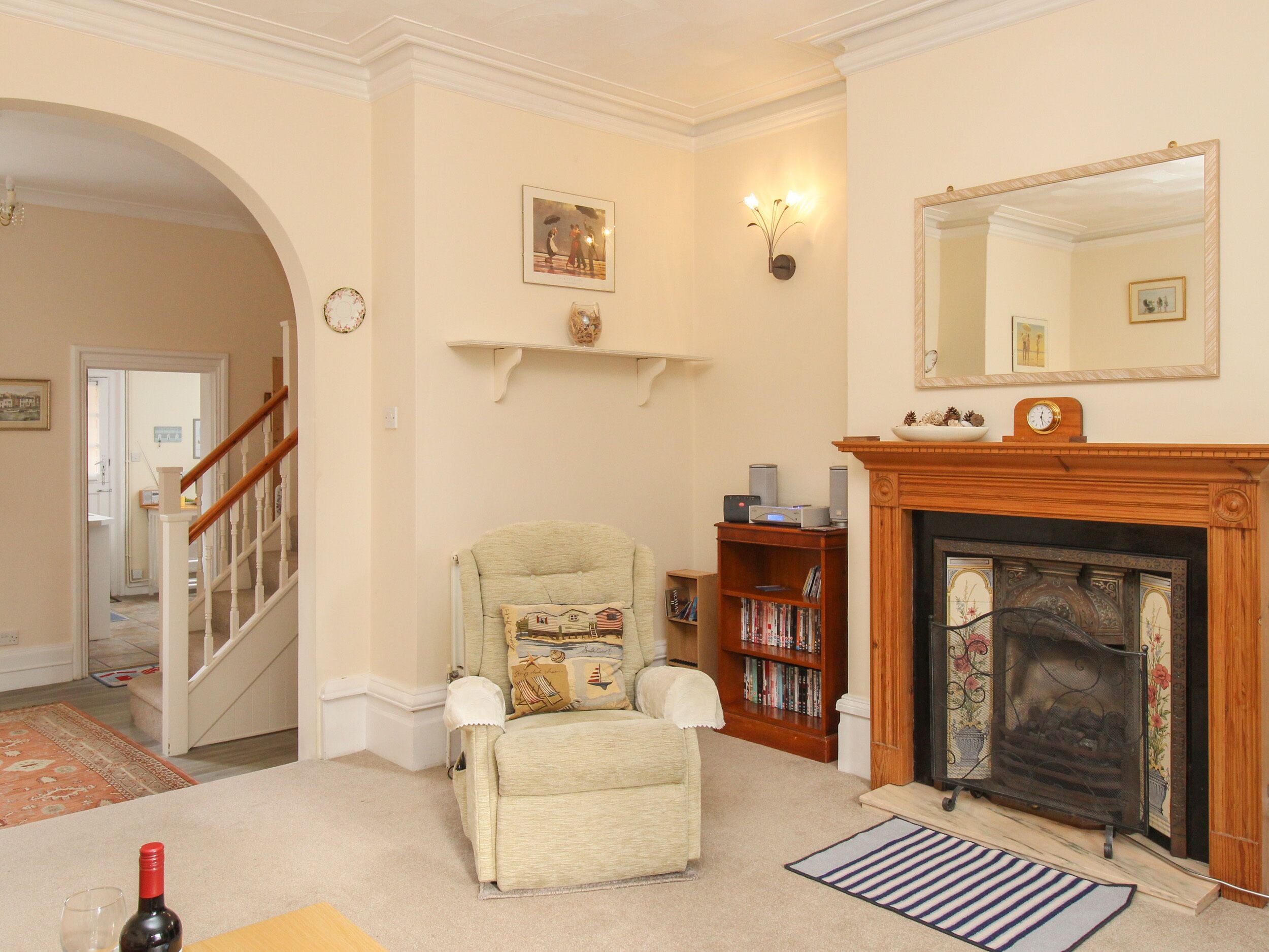 A living room with a fireplace, a bookshelf, a comfortable armchair, and a staircase leading to another room.