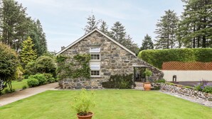 A stone house with a sloped roof, a well-maintained lawn, and a potted plant in the foreground.