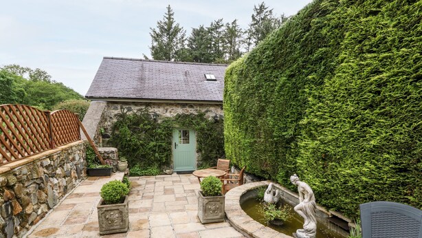 A stone patio with a wooden table and chairs, a small fountain, and a green door.