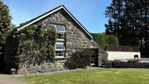 A stone building with a sloped roof, a small porch, and a well-maintained lawn.