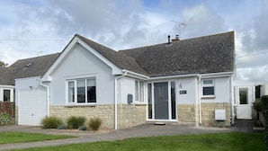 A two-story house with a grey tiled roof, a white front door, and a small front garden. - Shipton Hill View (Bridport)