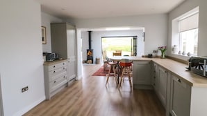 A modern kitchen with wooden flooring, a built-in stove, and a dining area with chairs. - Shipton Hill View (Bridport)