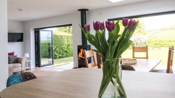 A modern living room with a glass table, a fireplace, and a view of the outdoors. - Shipton Hill View (Bridport)