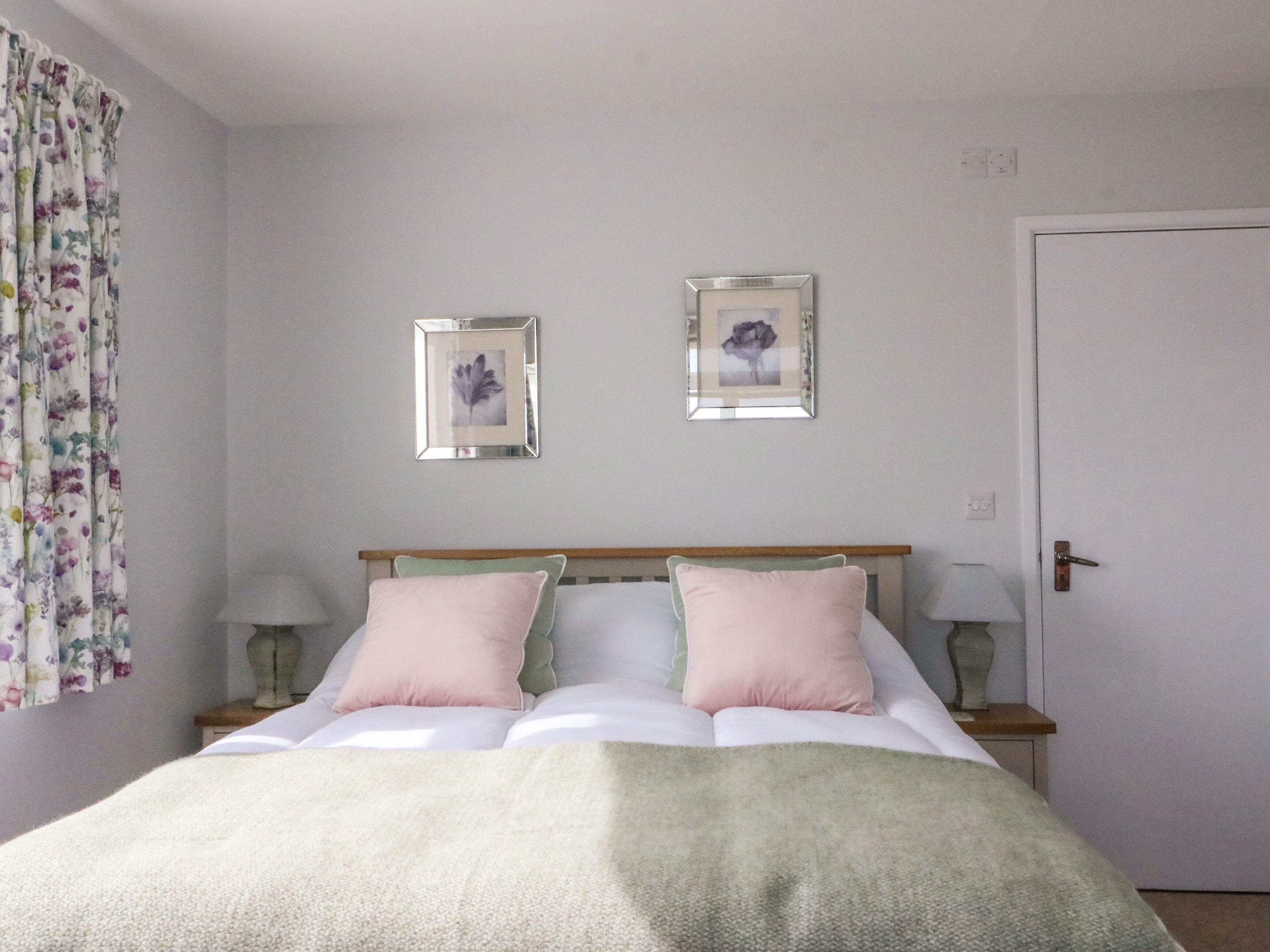 Une chambre à coucher avec un lit, deux tables de chevet, une porte et deux tableaux encadrés accrochés au mur.