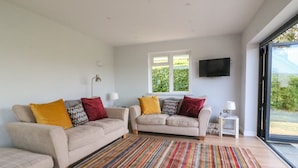 A living room with two sofas, a striped rug, a TV, and a window with a view of greenery. - Shipton Hill View (Bridport)