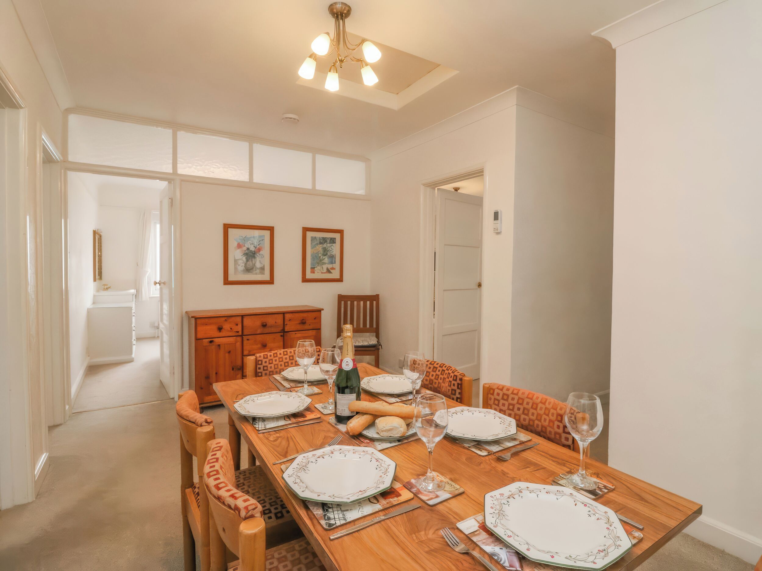 A dining room with a wooden table set for four, chairs, a chandelier, and artwork on the walls.