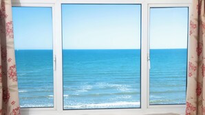 Een kamer met uitzicht op zee, te zien door een raam met gordijnen.