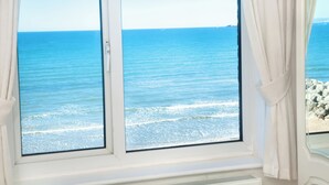 Een raam met uitzicht op zee, gordijnen en een stenen muur.