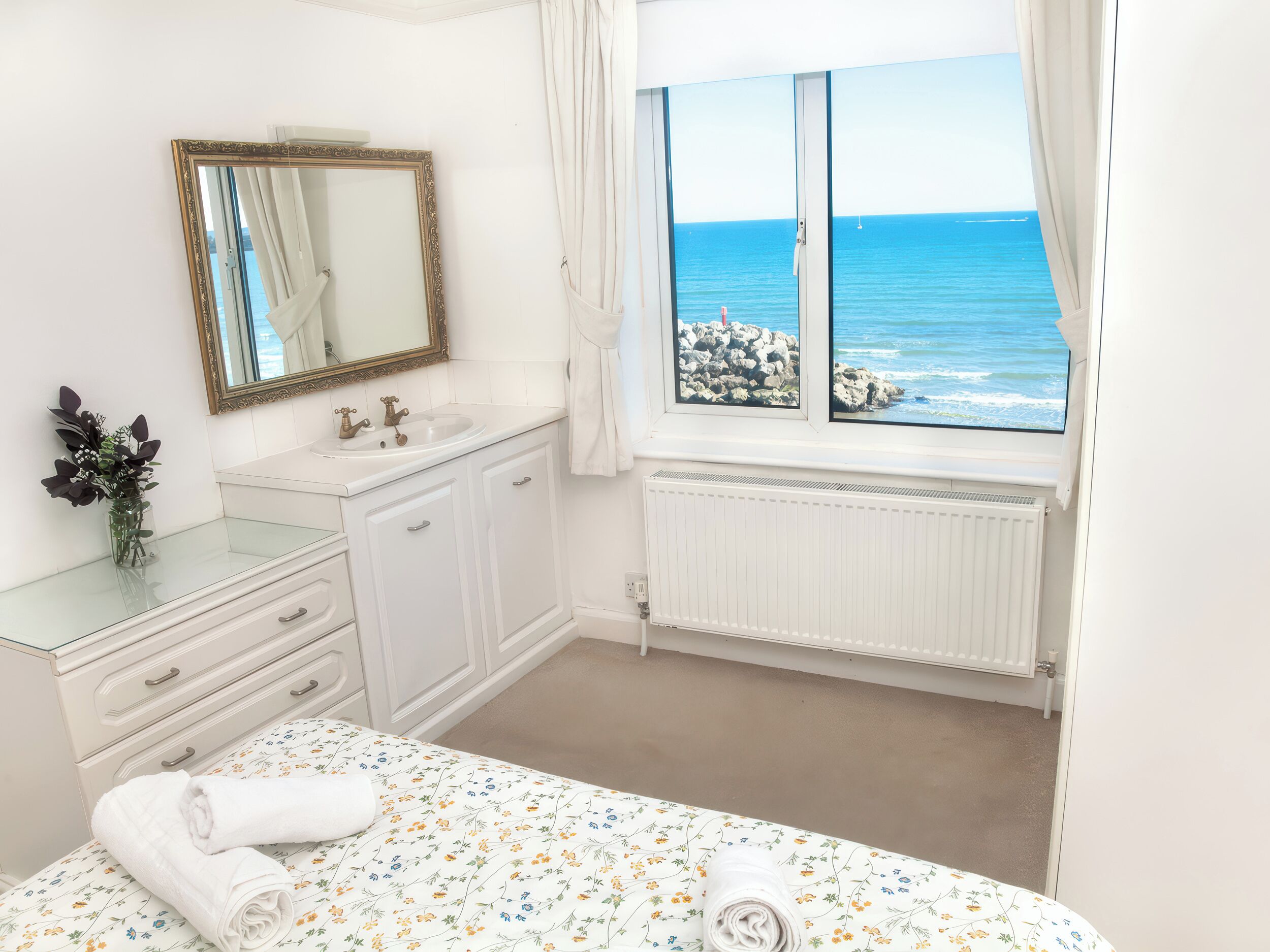 Un dormitorio con cama, un baño con lavamanos y espejo, y una ventana con vista al mar.