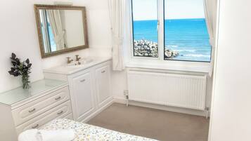 Un dormitorio con cama, un baño con lavamanos y espejo, y una ventana con vista al mar.
