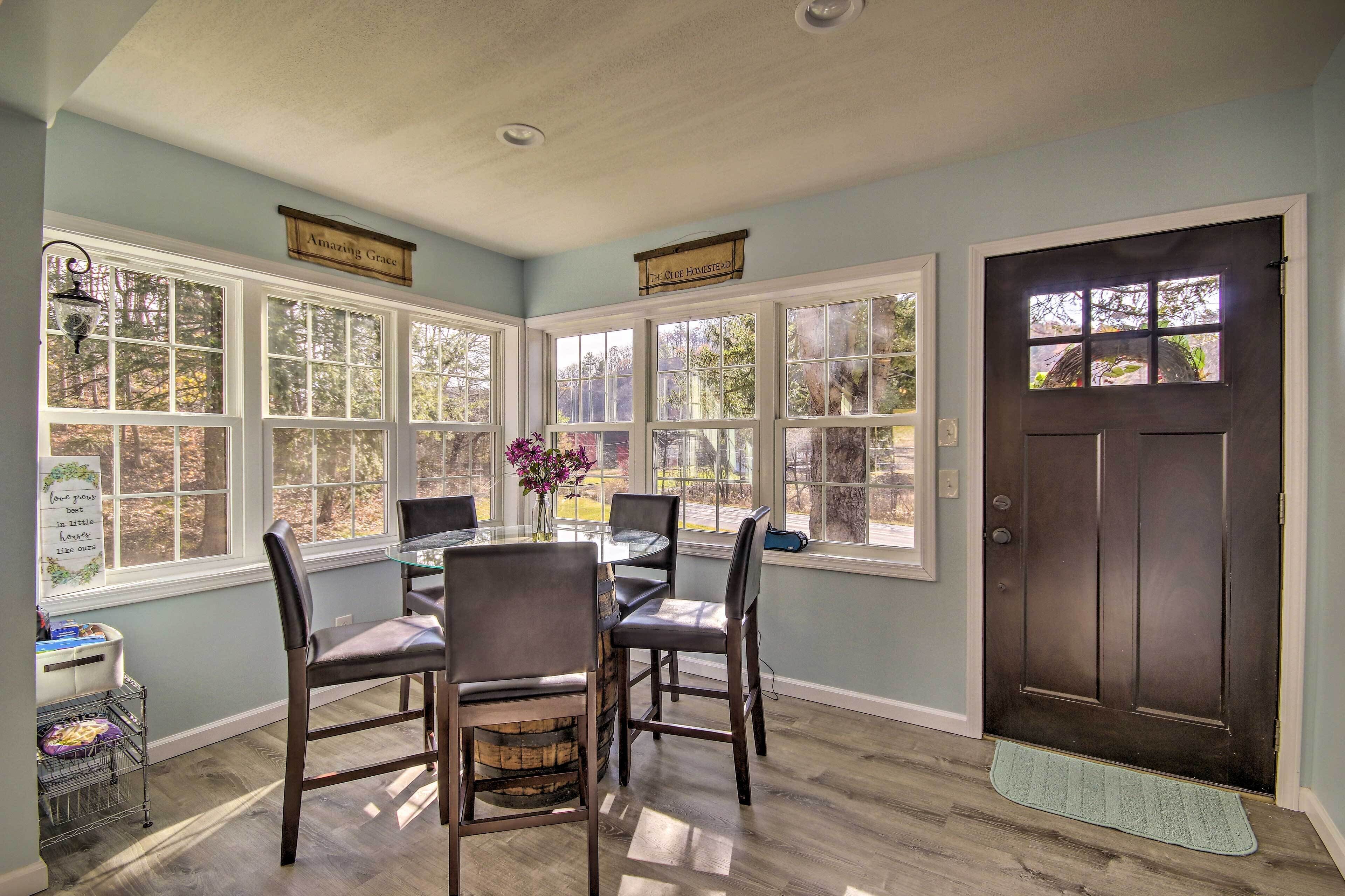 A dining area with a table and chairs, large windows, a dark door, and a small rug at the entrance.
