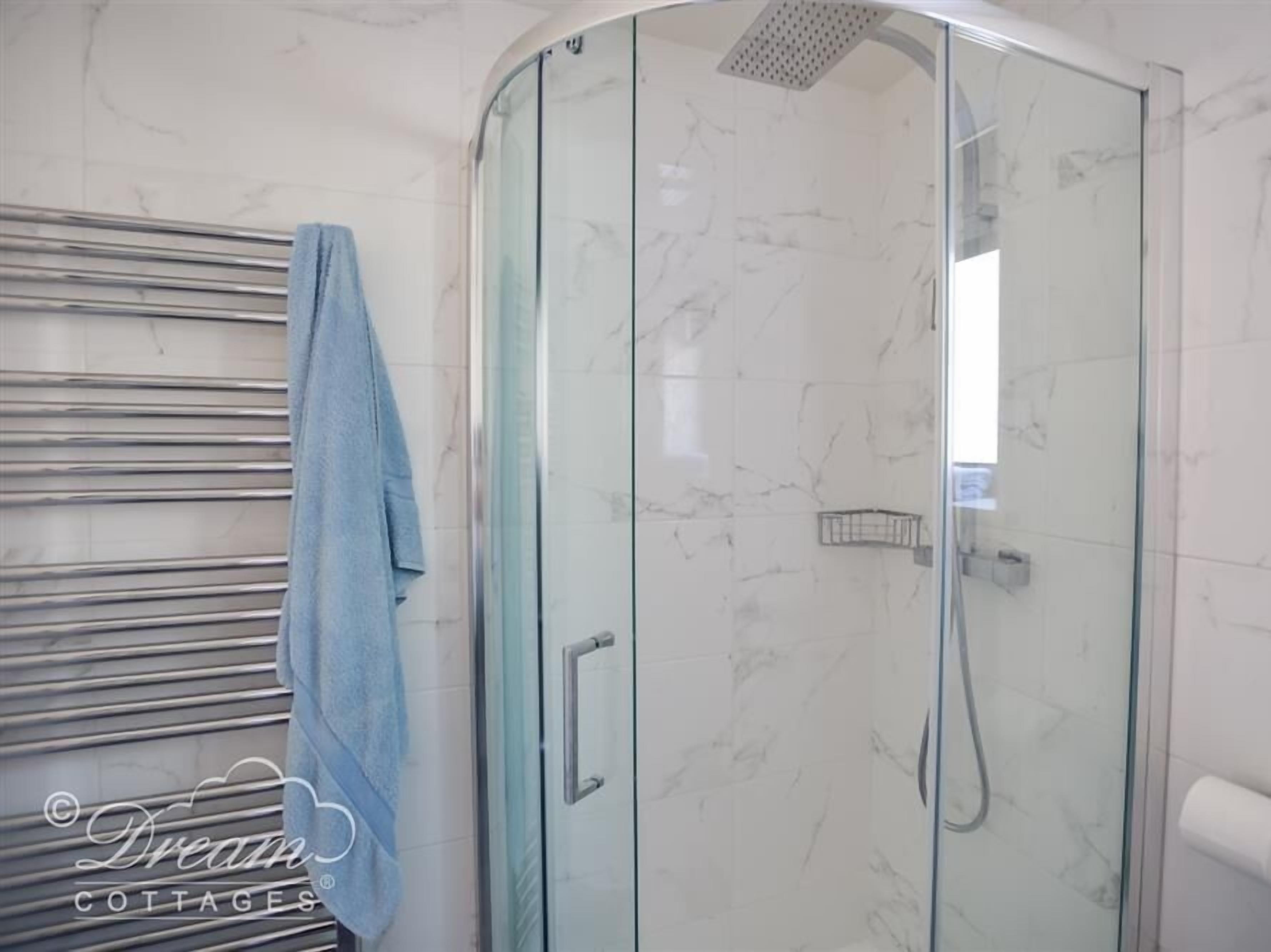 A glass-enclosed shower with a handheld showerhead and a towel rack with a towel.