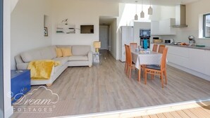 A modern living room with a sofa and a dining table set for four. - The Wave (Bridport)
