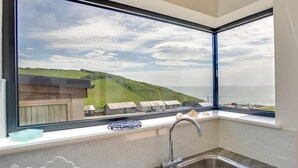 A kitchen with a large window overlooking a coastal landscape. - The Wave (Bridport)
