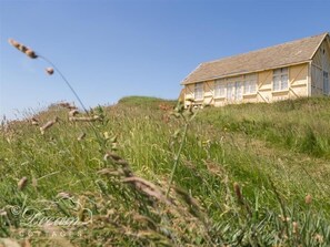 A cottage with a sloped roof, multiple windows, and a grassy field in the foreground. - The Wave (Bridport)