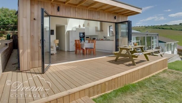 A modern, open-plan living space with a kitchen, dining area, and a deck. - The Wave (Bridport)