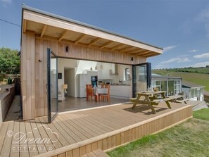 A modern, open-plan living space with a kitchen, dining area, and a deck. - The Wave (Bridport)