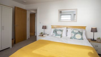 Un dormitorio con cama, lámparas de noche, mesita de noche con lámpara, espejo en la pared y una puerta que da a otra habitación.