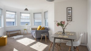 Een moderne woonkamer met een bank, een eettafel met stoelen, een bankje en een bijzettafeltje met een bloevas.