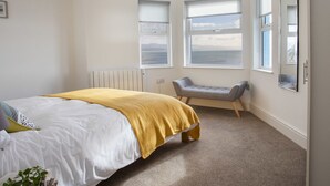 Een slaapkamer met een bed, een bankje en grote ramen met uitzicht op zee.