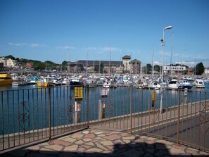 A marina with boats docked, a stone-paved walkway, and a building in the background.