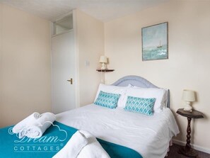 A bedroom with a bed, pillows, a nightstand, a lamp, a painting, and a towel on the bed.