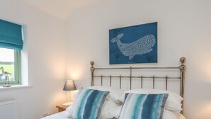 Una cama bien hecha con almohadas a rayas, una manta azul y una obra de arte en la pared con un borrego.