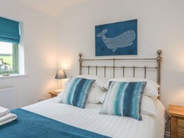 Una cama bien hecha con almohadas a rayas, una manta azul y una obra de arte en la pared con un borrego.