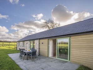 A stone building with a tiled roof, a patio with a table and chairs, and a green door. - Mynydd Parys (Llanfairpwllgwyngyll)