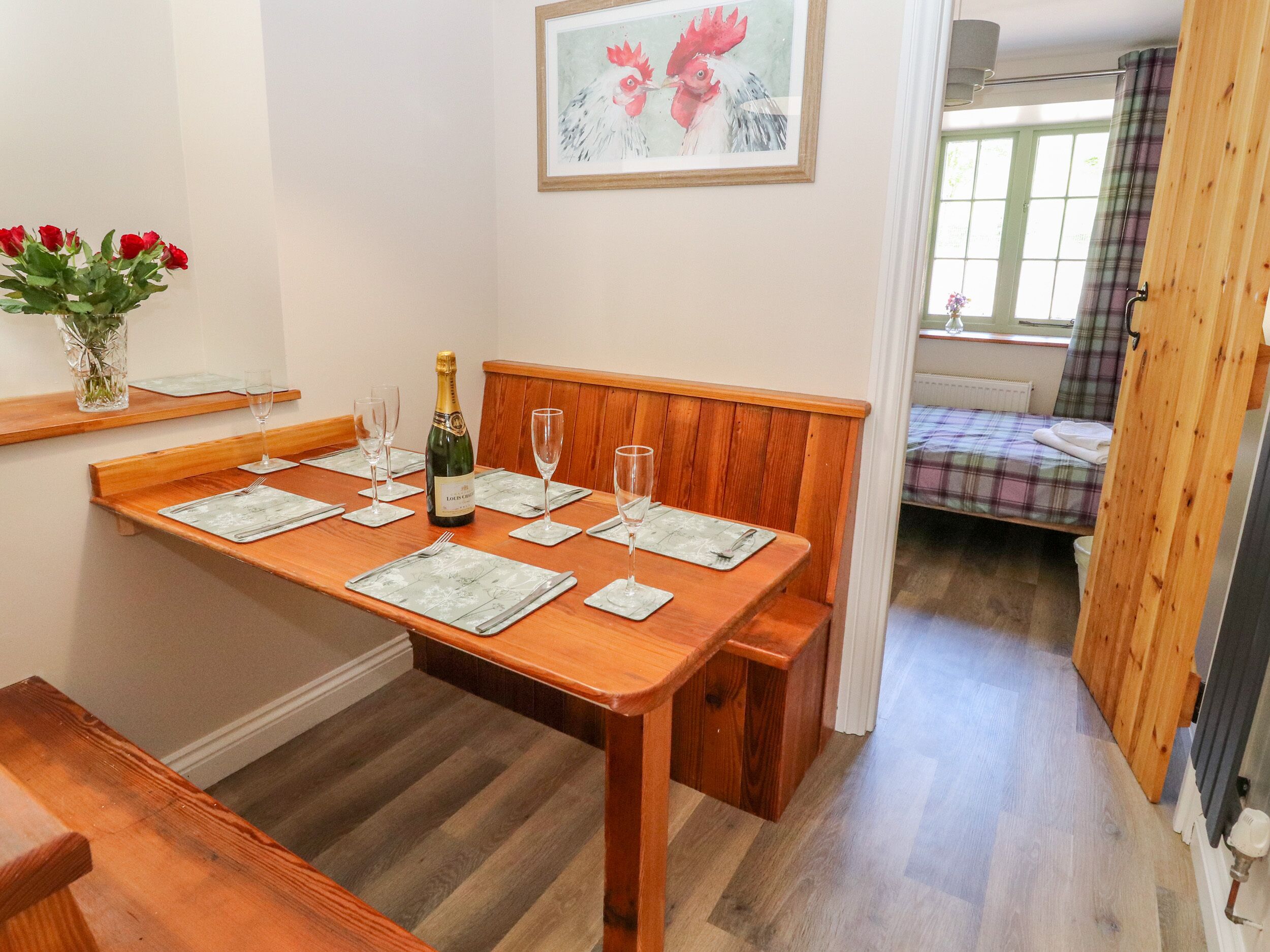 A dining area with a wooden table set for four, a bottle of champagne, and a framed artwork on the wall.
