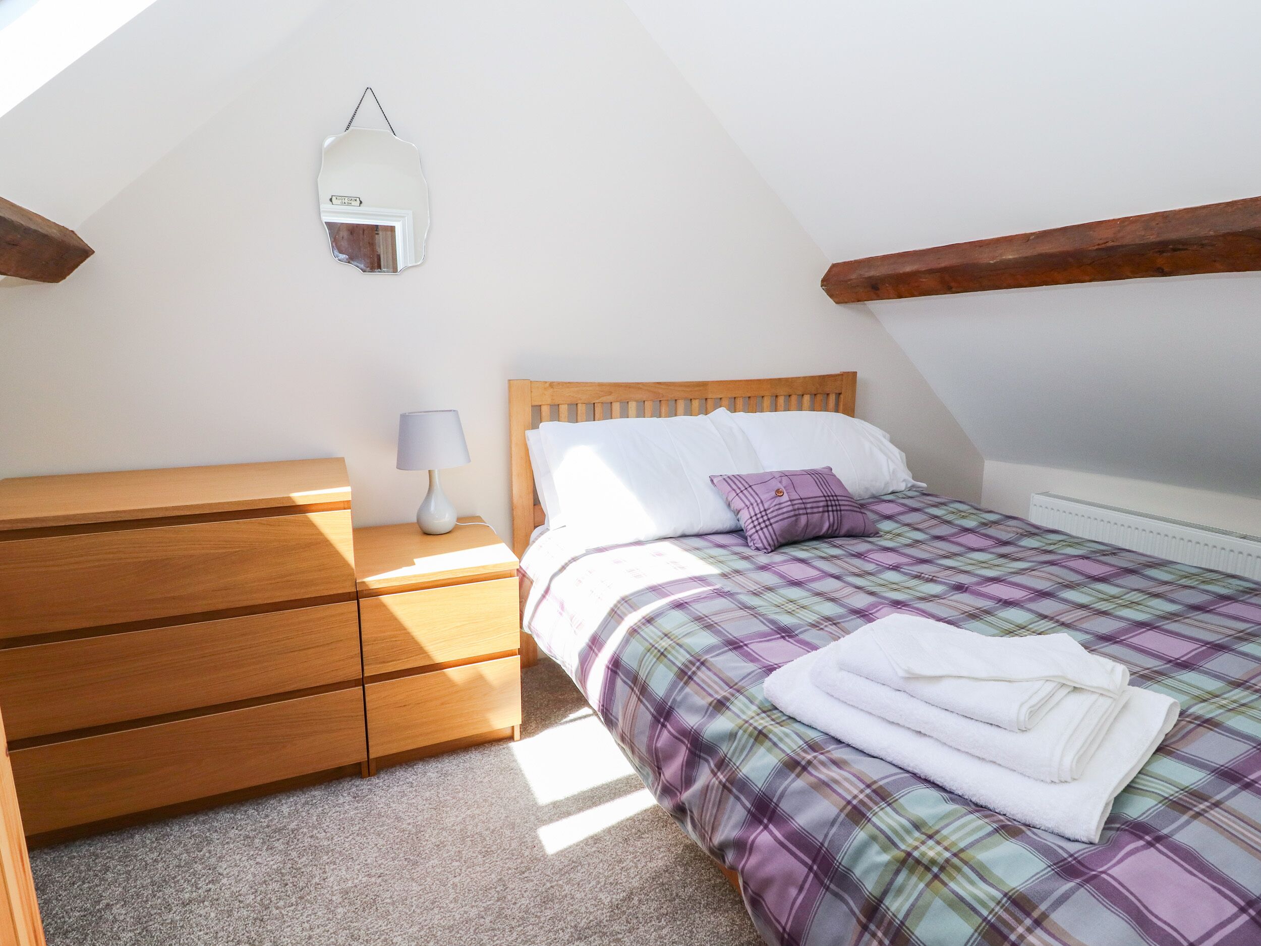 A bedroom with a wooden bed, a nightstand with a lamp, and a wall-mounted mirror.