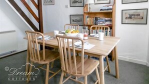 A dining area with a wooden table, four chairs, a bowl of fruit, and a bookshelf in the background. - Tavern Way (Wareham)