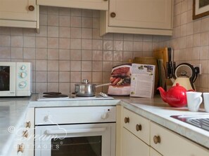 Una cocina con estufa blanca, microondas, tetera roja y libro de cocina sobre la encimera.