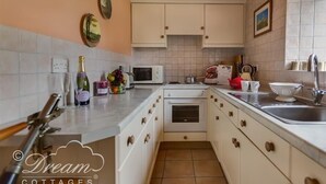 A compact kitchen with white cabinets, a microwave, a kettle, and a sink. - Tavern Way (Wareham)