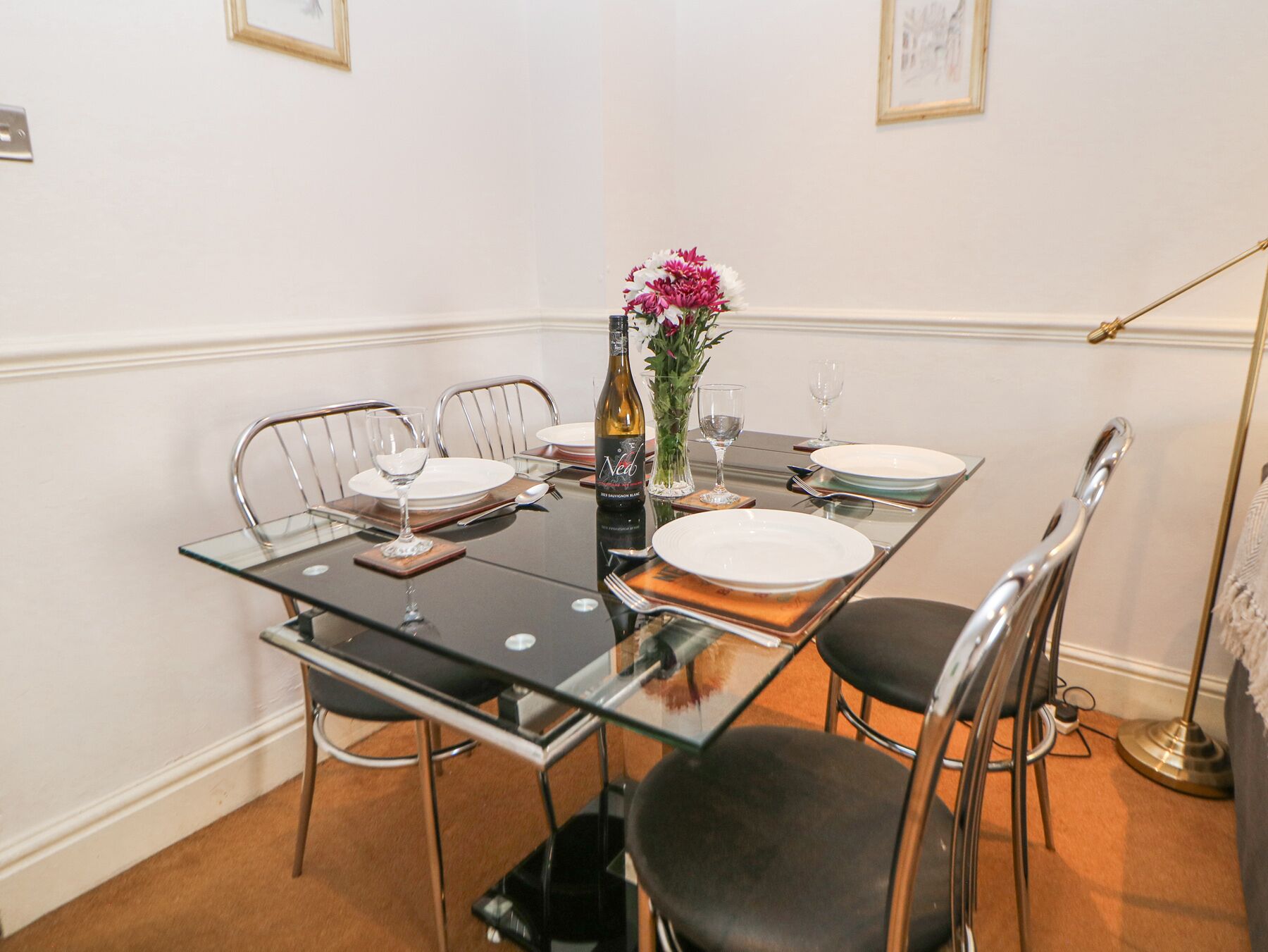 A dining table set with plates, cutlery, and a bottle of wine, surrounded by metal chairs.